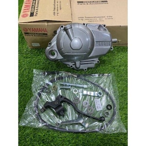 Puede incluir: Una cubierta de motor de motocicleta Yamaha gris y un kit de piezas se muestran sobre una superficie verde. El kit incluye una palanca negra, cables y varios componentes metálicos. Dos cajas de cartón con la marca Yamaha están en el fondo.