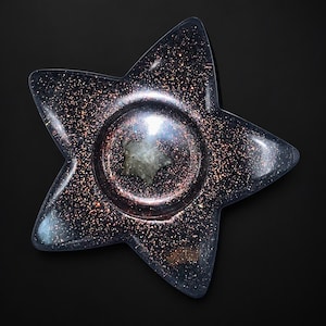 May include: A star-shaped tray made of dark, translucent resin embedded with fine copper-colored glitter particles. The center features a circular indentation containing a small, light-colored, star-shaped stone or inlay with a smooth surface.