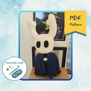 May include: A white ceramic mug with a black handle and the text "But First, Coffee" in a bold, black font. The mug is set against a blurred background. The mug is approximately 10 cm tall.