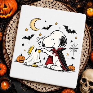 May include: A white square tile featuring a cartoon illustration of Snoopy dressed as a vampire touching the nose of Woodstock dressed as a ghost. The design includes a yellow crescent moon, black bats, orange pumpkins, a spider web, and the text Boop!