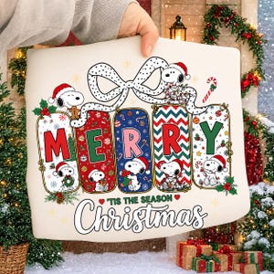 May include: A cream-colored sweatshirt featuring a graphic of Snoopy characters in five vertical panels spelling MERRY. The design includes a large polka-dot bow, candy canes, and holiday greenery. Below the panels, the text reads 'TIS THE SEASON Christmas.