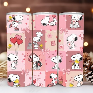 May include: A cylindrical tumbler featuring a repeating pattern of Snoopy and Woodstock in various activities against a pink patchwork background. The design includes hearts, bows, and the text XOXO and LOVE, rendered in shades of pink, white, and red.