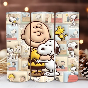 Peut inclure: Un gobelet cylindrique orné d'un collage de bandes dessinées Peanuts en arrière-plan. Le motif central représente Charlie Brown portant un t-shirt jaune à rayures noires en zigzag, serrant dans ses bras son chien blanc Snoopy et Woodstock.