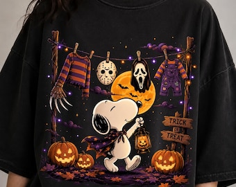 May include: A black t-shirt featuring a graphic of a white beagle wearing a purple cape and holding a lantern. Above, a clothesline displays a striped sweater with clawed sleeves, a hockey mask, a ghost mask, and purple overalls. Text reads TRICK OR TREAT.