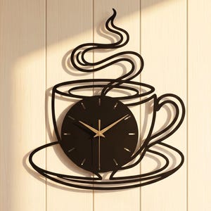 May include: A black metal wall clock shaped like a coffee cup on a saucer with rising steam. The circular clock face is integrated into the cup design, featuring thin gold hands and simple gold hour markers against a solid black background.