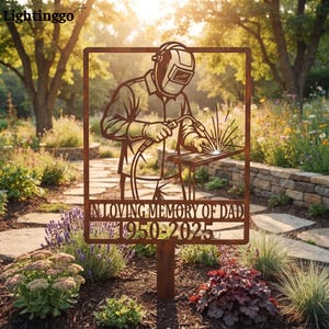 Op de afbeelding: Een rechthoekige metalen tuinpaal met een roestkleurige afwerking, voorzien van een uitgesneden silhouet van een lasser met een helm en een toorts. De tekst "IN LOVING MEMORY OF DAD" en "1950-2025" is onderaan in het metaal gelaserd.