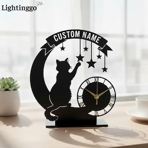 May include: Black cat-themed desk clock with a crescent moon and star design. The clock features a silhouette of a cat reaching for hanging stars, with a clock face below. The banner above reads "CUSTOM NAME".