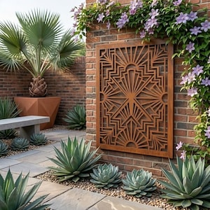May include: A rectangular metal wall panel featuring a geometric Art Deco sunburst pattern with radiating lines and angular shapes. The panel has a rusted brown finish and is mounted on a red brick wall surrounded by green plants and flowers.
