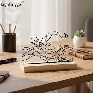 May include: A black line art swimmer figure in the water, mounted on a wooden base. The swimmer is wearing goggles and a cap. The name "Williams" is displayed on the base. The logo "Lightinggo" is in the top left corner.