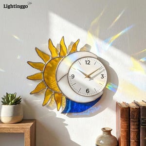 May include: A decorative wall clock featuring a sun and moon design. The sun is yellow, the moon is white, and the clock face is white with gold hands. The clock is mounted on a white wall.