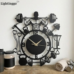 May include: Black metal wall clock with a fitness theme. The clock features a silhouette of a weightlifter, barbells, dumbbells, kettlebells, and other gym equipment. The clock hands are gold. The brand name "Lightinggo" is in the top left corner.