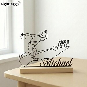 May include: A black metal bowling-themed sculpture with the name "Michael" on a wooden base. The sculpture depicts a bowler in motion, a bowling ball, and pins. The "Lightinggo" logo is in the top left corner.