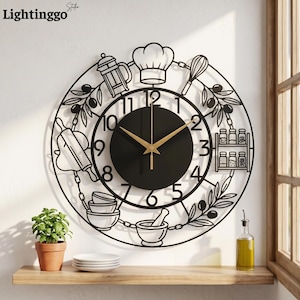 May include: A circular black metal wall clock featuring a central black dial with gold hands and numbers 1 through 12. The outer frame displays kitchen-themed silhouettes including a chef hat, whisk, rolling pin, mortar, pestle, and spice rack.