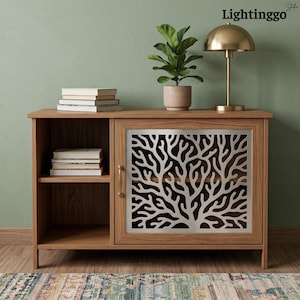 May include: A wooden cabinet with an open shelf containing a stack of books and a single door featuring a silver-toned metal panel with a cut-out coral branch pattern. A gold-toned lamp and a potted plant sit on top. Text reads Lightinggo.