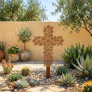 May include: A decorative brown metal cross with a floral pattern, displayed in a garden setting. The cross is embellished with cut-out flowers and foliage. The garden includes succulents and small trees, set against a beige wall.