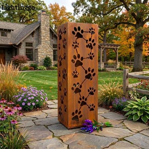 May include: A tall, rectangular, rust-coloured metal garden lantern featuring laser-cut paw print patterns on its sides. The structure has a weathered, oxidised finish and is designed to allow light to shine through the cutouts.