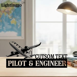 May include: Black metal airplane silhouette with the text "CUTSOM TEXT PILOT & ENGINEER". The image also includes the text "Lightinggo Studio". The airplane is on a wooden surface.
