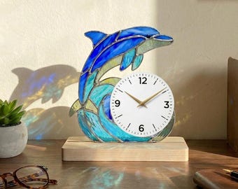 May include: A stained glass dolphin clock with a white clock face and gold hands. The dolphin is blue and turquoise, mounted on a wooden base. The clock is approximately 20 cm tall.
