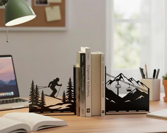 May include: Black metal bookends with a skier and mountain scene design. One bookend features a skier on a slope with trees, the other depicts a mountain with a ski lift. The bookends are on a wooden desk with books.