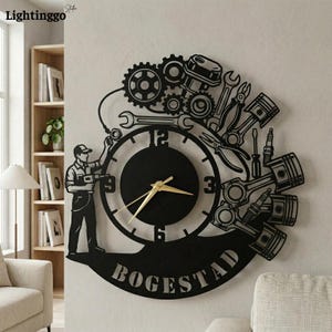 May include: Black metal wall clock featuring a mechanic silhouette, gears, pistons, and tools. The clock has gold hands and the word "BOGESTAD" at the bottom. The clock is approximately 24 inches in diameter.
