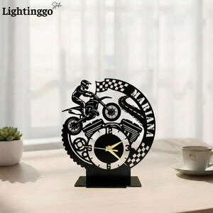 Könnte beinhalten: Schwarze dekorative Uhr mit einem Motocross-Fahrer auf einem Motorrad, mit dem Namen "Mariana" und einem karierten Flaggen-Design. Die Uhr hat goldene Zeiger und einen schwarzen Sockel. Der Markenname "Lightinggo" befindet sich in der oberen linken Ecke.