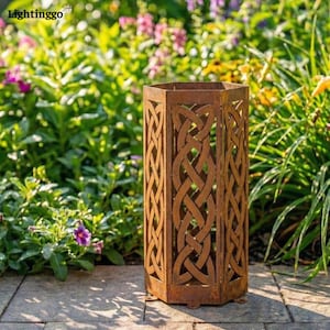 May include: A hexagonal, rusty brown metal outdoor lantern with Celtic knotwork cutouts. The lantern is set on a stone patio, surrounded by lush green foliage and colorful flowers, creating a garden accent.