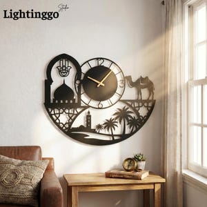 May include: Black metal wall clock with an Islamic design. The clock features a mosque, palm trees, a camel, and a Hamsa hand. The clock hands are gold. The text "Lightinggo Studio" is in the upper left corner.