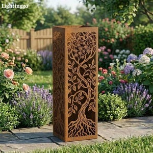 May include: A tall, rectangular, rusty-brown metal planter with a tree design cut out of the sides. The tree features roots, a trunk, branches, leaves, and flowers. The planter is in a garden setting with flowers and greenery.