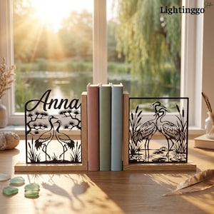 May include: A pair of wooden bookends featuring black metal cutouts of cranes in a marsh setting. The left piece displays the name Anna in script lettering above two cranes, while the right piece shows two cranes among reeds and water lilies.