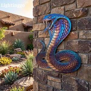 May include: A metal wall art piece shaped like a cobra snake with an iridescent finish that shifts between blue, purple, and bronze tones. The snake is depicted in an upright, coiled position with its hood flared and mouth open, revealing fangs.