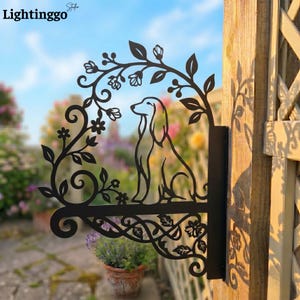 May include: Black metal dog silhouette sign with floral and leaf accents. The sign features a sitting dog within a decorative frame, perfect for garden or home decor. The sign is mounted on a wooden post.