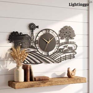 May include: A black metal wall clock featuring a farm scene with a barn, a windmill, a tree, and grazing cows. The clock face has gold-colored hands and numbers. The text Lightinggo is visible in the top right corner of the image.