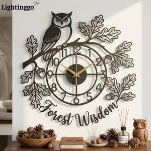 Puede incluir: Un reloj de pared negro con un diseño recortado de un búho posado en una rama de roble con hojas y bellotas. La esfera circular tiene manecillas doradas y números del uno al doce. El texto Forest Wisdom aparece en letra cursiva debajo.