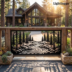 May include: A black metal decorative railing panel featuring a laser-cut design of a winding river flowing through a dense pine forest. The panel is mounted within a wooden frame, casting a detailed shadow of the forest scene onto the stone patio.