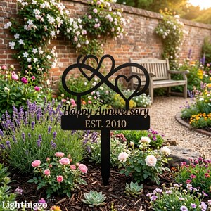 Peut inclure: Piquet de jardin en métal noir avec un symbole infini et deux cœurs. Le piquet porte l'inscription "Happy Anniversary EST. 2010" et est entouré de fleurs et de verdure.