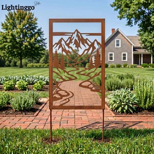 May include: A rectangular, rusty brown metal garden art piece featuring a mountain and river scene. The design is cut out, creating a silhouette of trees, mountains, and a winding river. The art is supported by two stakes.