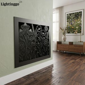 May include: A rectangular black metal fireplace screen featuring a laser-cut floral design. The intricate pattern displays various wildflowers, including daisies and poppies, with slender stems and leaves. The screen is mounted on a light green wall.