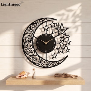 May include: A black wall clock featuring a crescent moon shape with intricate scrollwork patterns and a cluster of stars. The circular clock face is black with gold-colored hands and numerals at 3, 6, 9, and 12 o'clock positions.