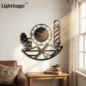 Peut inclure: Horloge murale en métal noir sur le thème du salon de coiffure. L'horloge représente un fauteuil de barbier, des ciseaux, un peigne, un rasoir droit et un poteau de barbier. Les aiguilles de l'horloge sont de couleur marron clair. Le texte "Lightinggo Studio" est en haut à gauche.