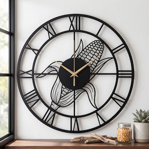 May include: A large circular wall clock featuring a black metal frame with Roman numerals and a central cutout design of a corn cob. The clock has thin gold-colored hands mounted on a solid black circular center piece, creating a contrast.