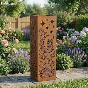 May include: A tall, rectangular, weathered metal garden sculpture. The brown sculpture features cut-out designs of stars, a crescent moon, butterflies, and floral patterns. The sculpture is placed in a garden setting with flowers and greenery.