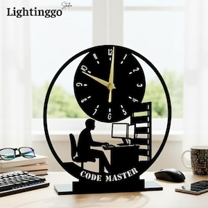 May include: Black desk clock with a circular design. The clock features a silhouette of a person at a computer, with the words "CODE MASTER" at the base. The clock hands are gold.