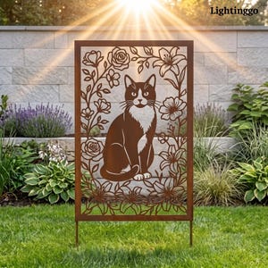 May include: A rectangular metal garden screen featuring a laser-cut silhouette of a seated cat surrounded by a detailed floral border of roses and lilies. The panel has a rusted brown finish and is supported by two thin metal stakes in the grass.
