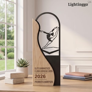 Op de afbeelding: Een verticale trofee met een licht houten paneel met een gebogen rand en een zwart metalen gedeelte. Het zwarte gedeelte toont een uitgesneden silhouet van een turner op de vloer. Tekst: ELITE GYMNASTICS FLOOR EXERCISE OPEN 2026 PREMIER CHAMPION.