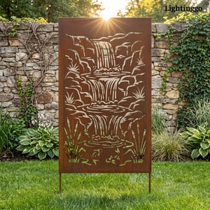 May include: A rectangular, rust-colored metal garden screen featuring a laser-cut design of a multi-tiered waterfall cascading over rocks, surrounded by stylized reeds and two fish at the base. The panel is supported by two thin metal stakes.