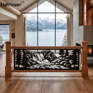 May include: A black metal railing insert featuring a laser-cut landscape design of a waterfall surrounded by pine trees. The rectangular panel is framed by natural wood posts and a top rail, positioned in front of a large window with a mountain view.