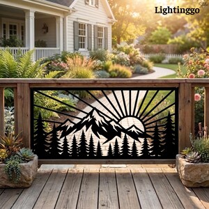 May include: A black metal decorative railing panel featuring a laser-cut design of a mountain range, a forest of pine trees, and a sunburst pattern. The rectangular panel is installed between wooden posts on a deck, with stone planters nearby.
