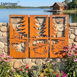 May include: Three rectangular metal panels with a rust-colored finish, featuring laser-cut silhouettes of a lakeside scene. The design includes a log cabin, pine trees, a boat at a dock, cattails, swimming fish, and birds flying in the sky.