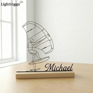 May include: A black metal windsurfer sculpture with the name "Michael" in cursive script on a wooden base. The sculpture depicts a person windsurfing with a sail and board. The sculpture is a decorative item.