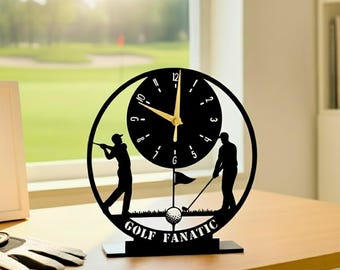 May include: Black golf-themed desk clock with a circular design. The clock features silhouettes of golfers, a golf ball, and the words "GOLF FANATIC." The clock hands are gold, and the clock face is black.